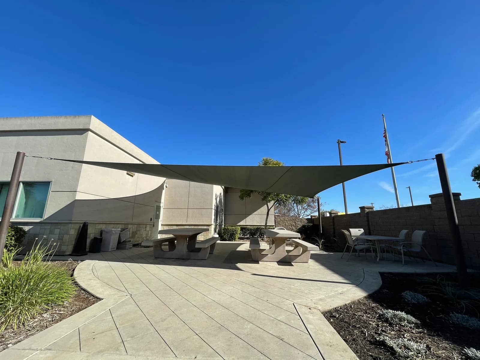 Shade sails over a paved community courtyard with benches and walkway
